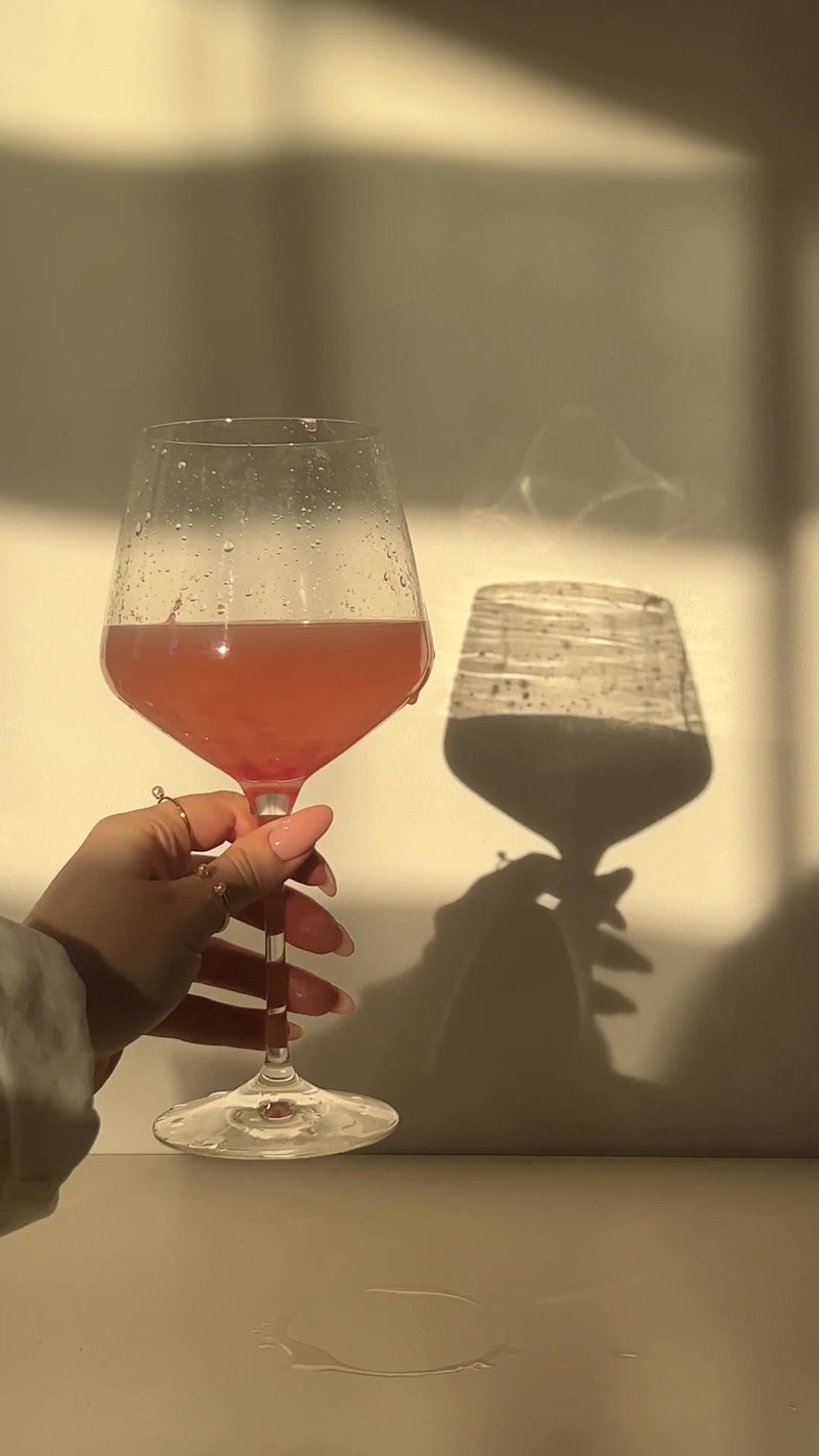 Hand holding a glass of pink supplement drink with a shadow on a light background